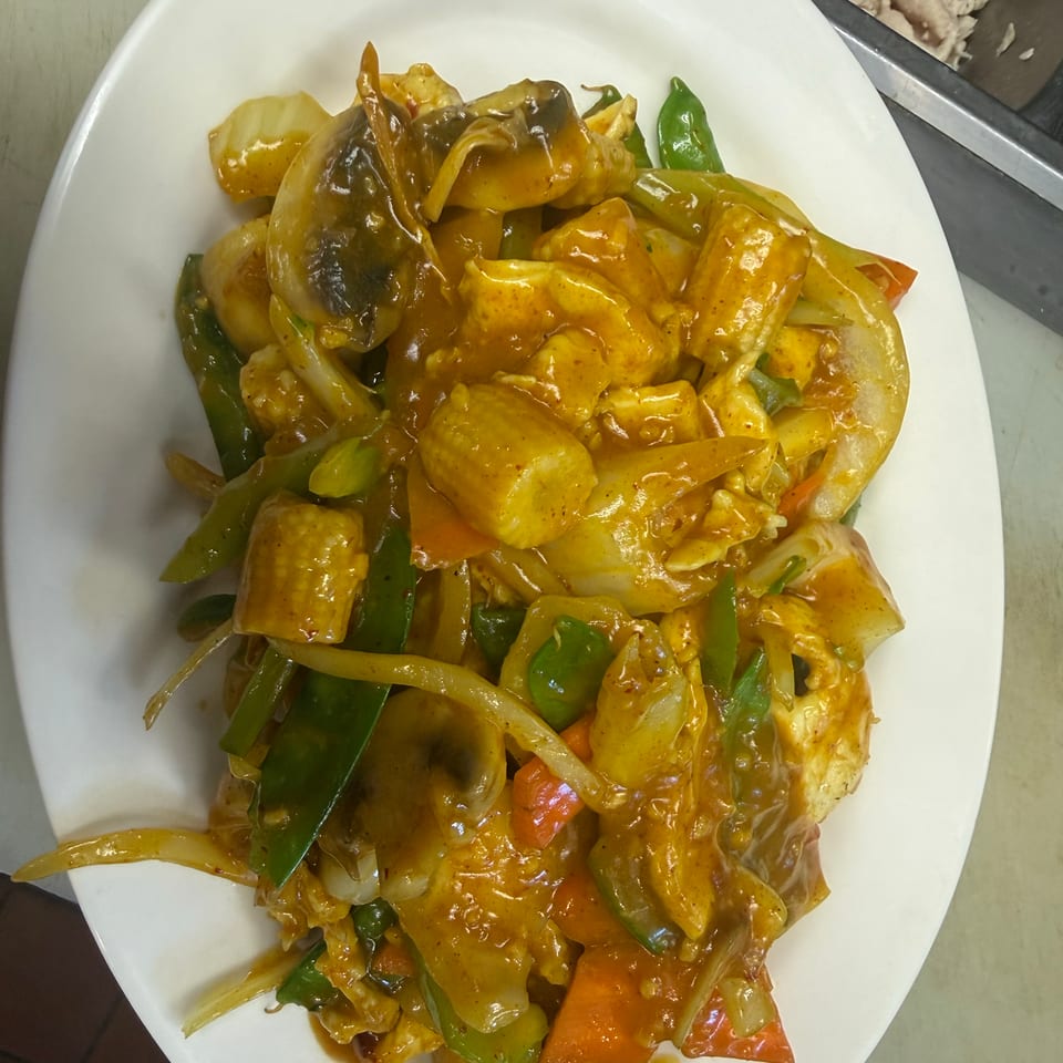 Plate of saucy stir-fried chicken with potatoes, bell peppers, onions, tomatoes, and mixed vegetables.
