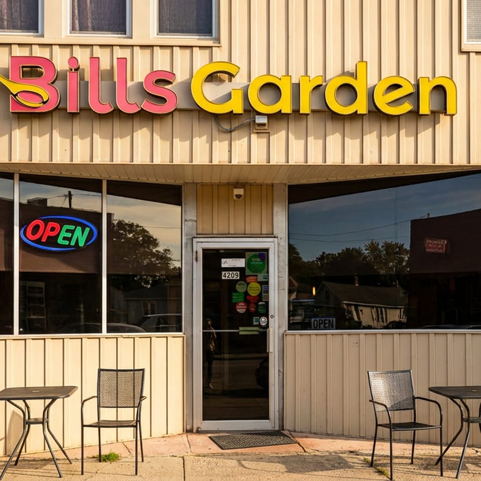 Exterior of Bill's Garden restaurant with colorful sign, open neon signs, glass entrance, and outdoor tables and chairs.