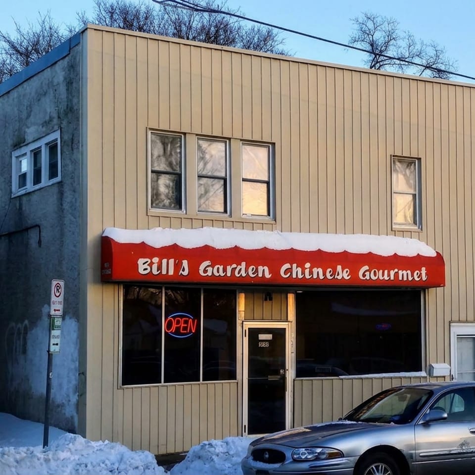 Snow-covered storefront for Bill's Garden Chinese Gourmet, featuring a red awning, neon open sign, and parked car.
