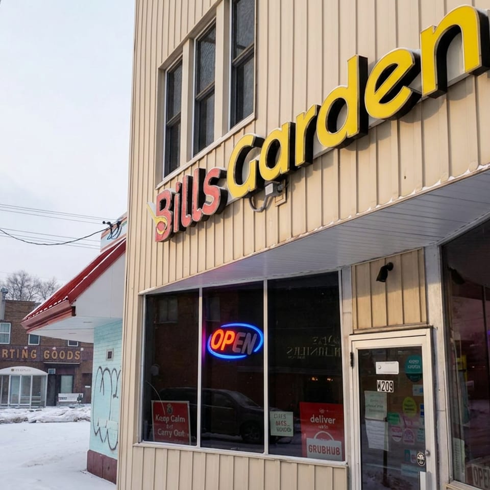 Snowy street view of Bill's Garden restaurant exterior with yellow signage, glowing open sign, and storefront windows.