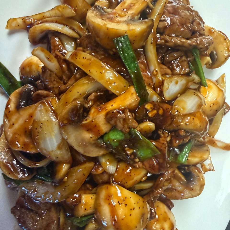 Glazed stir-fried beef with assorted mushrooms, onions, and green peppers on a white plate.