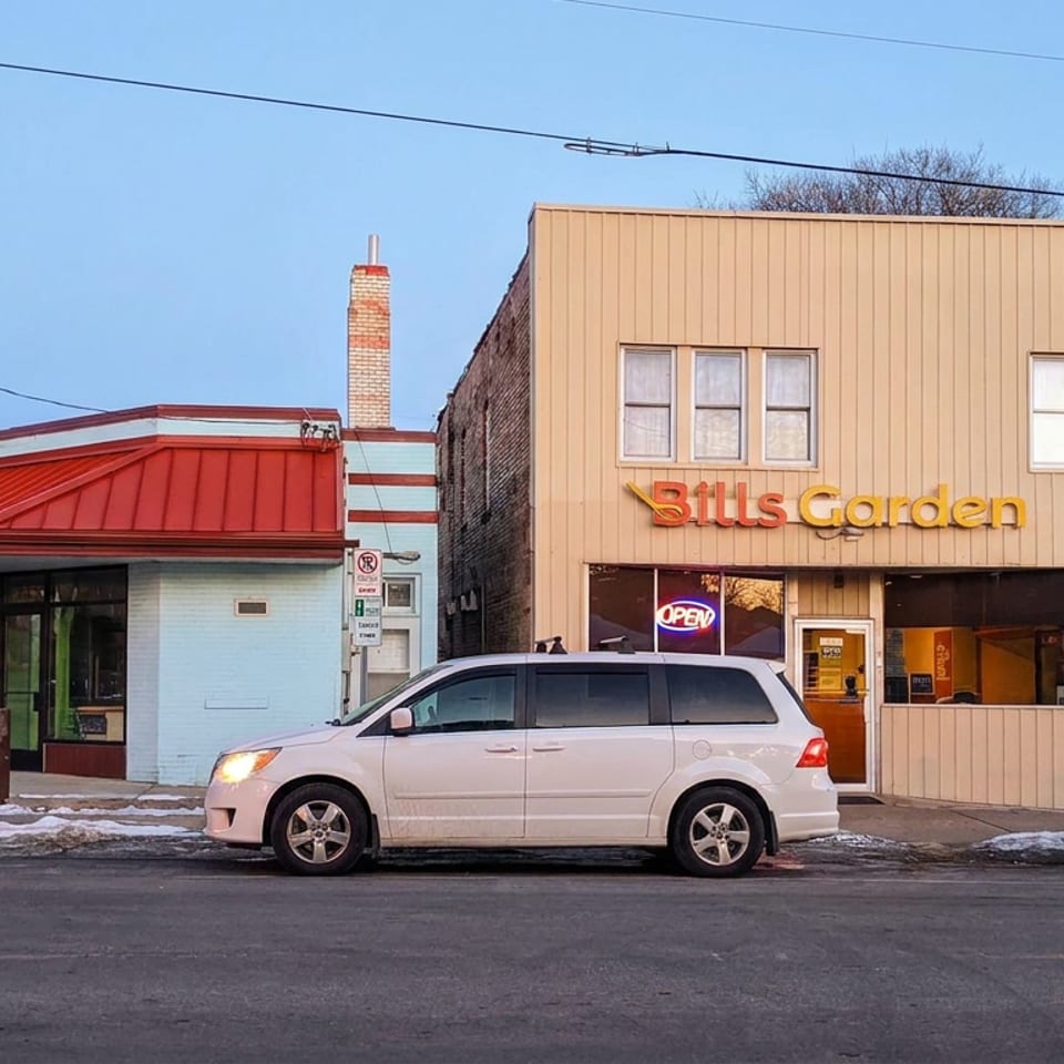 Street view of Bills Garden restaurant with tan facade, red roof, open sign, parked cars, and a colorful bird mural.