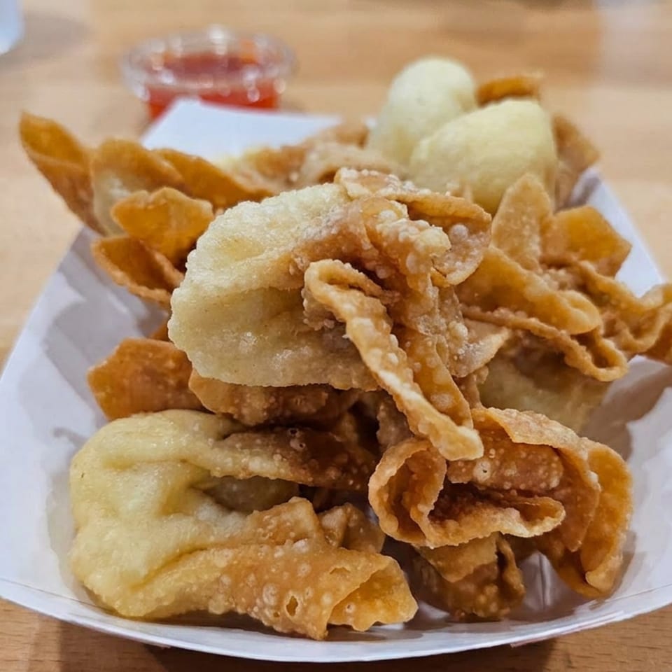 Plate of assorted golden fried dumplings or pastries with pale green scoops and red dipping sauce on a wooden table.